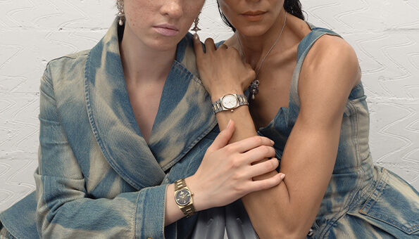 Two women modelling new-in Vivienne Westwood watches and jewellery in textured blue and brown outfits